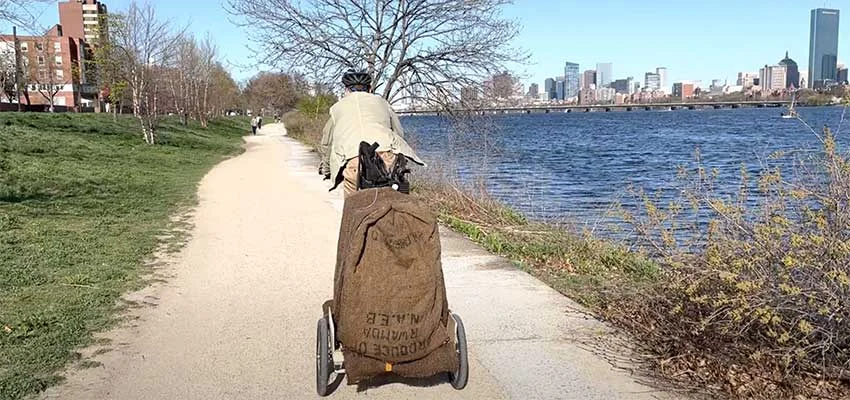 An earlier prototype: a rider towing the trailer with a jute sack over the load and no canopy, along the Charles River