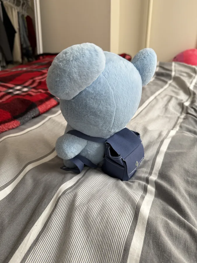 A plush doll seen from behind, wearing the small backpack enclosure