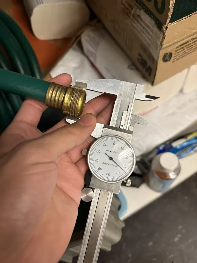 A hand holding a garden hose's brass fitting against a dial caliper