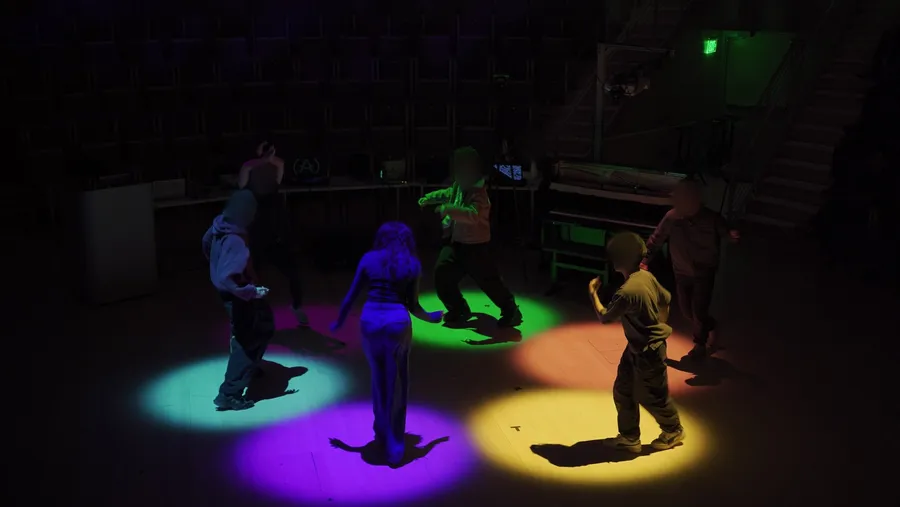 Dancers in the Encypher cypher in Tull Concert Hall, each standing in a colored pool of light, blurred